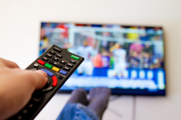 Close-up macro of man’s hand with TV remote control watching a soccer match